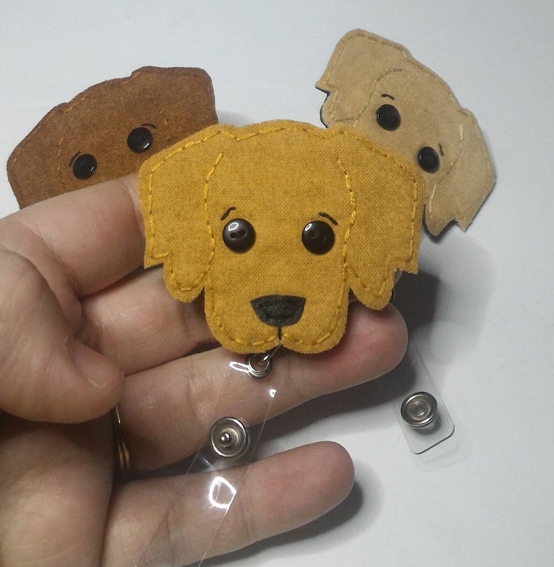 May include: Three felt dog badge holders with a clear plastic retractable badge reel. The dogs are brown, tan, and yellow.