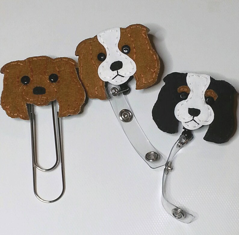 May include: Three felt dog badge holders. One brown dog with a clip, one brown and white dog with a retractable badge reel, and one black and white dog with a retractable badge reel.