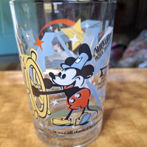 May include: Clear glass featuring Mickey Mouse in a vintage design. Mickey is depicted in his classic outfit, holding a ship's wheel. The glass has text that reads "Mickey 1928's Steam Boat Willie" and "...it was all started by a mouse."