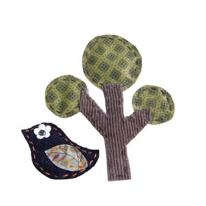 May include: Appliqué of a tree and bird. The tree has a brown corduroy trunk and three green patterned leaves. A dark blue bird with a white flower and leaf detail is next to the tree. The bird has orange stitching.