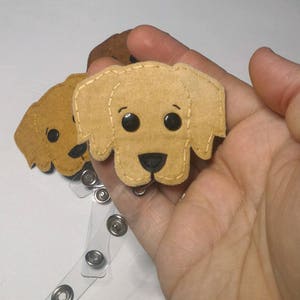 May include: A brown felt dog face with black eyes and a black nose attached to a clear plastic badge holder with silver metal rings.