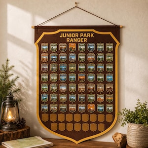 May include: A brown felt wall banner with yellow trim featuring the text JUNIOR PARK RANGER at the top. The banner displays a grid of embroidered patches representing various national parks, with empty shield-shaped spaces at the bottom.