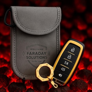 Puede incluir: Una funda gris para dispositivos móviles Faraday Solutions con un mosquetón negro junto a un mando de coche negro y dorado. El mando tiene botones para bloquear, desbloquear y otras funciones. El fondo es rojo borroso.