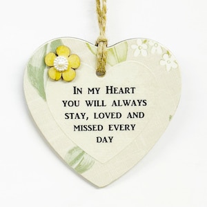 Può includere: Ornamento in legno a forma di cuore con un design floreale e la scritta "IN MY HEART YOU WILL ALWAYS STAY, LOVED AND MISSED EVERY DAY." Un fiore giallo con un centro di perle adorna l'angolo in alto a sinistra. Un cordino di iuta è attaccato per appenderlo.