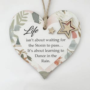 Może przedstawiać: Drewniana dekoracja w kształcie serca z kwiatowym wzorem i napisem „Life isn't about waiting for the Storm to pass... It's about learning to Dance in the Rain”. Dołączone są dwie drewniane gwiazdki.
