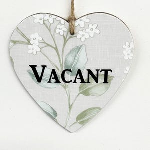 May include: A heart-shaped sign with a floral pattern in shades of green and white. The sign says "VACANT" in black letters.