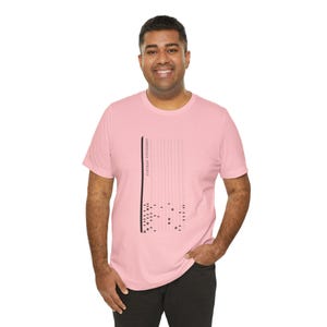 May include: A light pink short-sleeved t-shirt featuring a black graphic design on the chest. The graphic consists of vertical lines and a series of small black rectangles arranged in a pattern, with the text "FORTRAN STATEMENT" printed vertically.