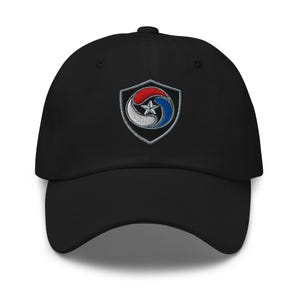 May include: A black baseball cap featuring an embroidered shield emblem on the front. The shield contains a circular design with red, white, and blue curved segments surrounding a central silver star, all outlined in a silver-toned thread border.