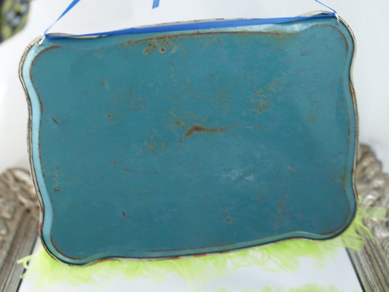 May include: A turquoise blue metal tray with a scalloped edge and a light green fringe around the bottom.