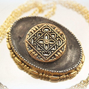 Peut inclure: Un collier avec un pendentif ovale en or et argent, au design orné et détaillé. Le pendentif présente un motif géométrique noir et or.