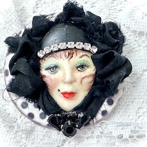 Könnte beinhalten: Eine schwarz-weiße Polka-Dot-Anstecknadel mit einem bemalten Gesicht, das einen schwarzen Schleier und ein Strass-Stirnband trägt.