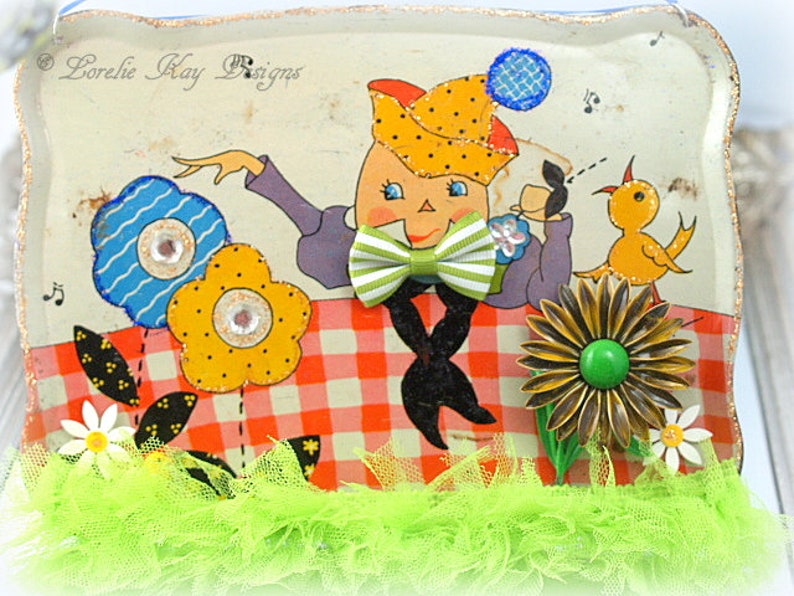 May include: A vintage tin tray with a whimsical illustration of a cartoon character wearing a hat and bow tie, holding a cup. The character is surrounded by flowers and a bird. The tray has a red and white checkered pattern and is decorated with green, blue, and yellow accents. The text "Lorelie Kay Designs" is visible in the top left corner.