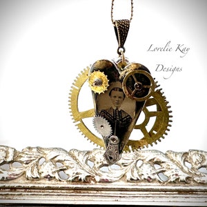 May include: A heart-shaped pendant necklace with a vintage photograph of a woman inside. The heart is decorated with gold gears and other steampunk-style embellishments. The necklace is hanging from a gold chain.