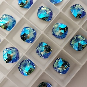 May include: A white plastic tray filled with 20 square-shaped blue rhinestones. The rhinestones have a light blue color with a green iridescent shimmer.