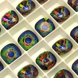 May include: A close-up view of a tray of iridescent, multi-colored, square-shaped rhinestones. The rhinestones are arranged in rows and columns in a white tray.