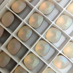 以下が含まれることがあります： 虹色の白い正方形のラインストーンが詰まった白いプラスチック製の箱