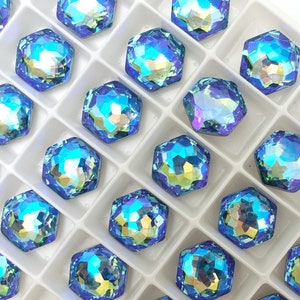 May include: A close-up view of a white plastic tray filled with iridescent blue hexagonal rhinestones. The rhinestones are arranged in rows and columns, creating a repeating pattern.