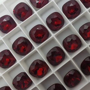 May include: A white plastic tray filled with red, faceted, square-shaped rhinestones.