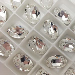 Puede incluir: Un contenedor de plástico transparente lleno de piedras de cristal ovaladas transparentes. Las piedras de cristal están dispuestas en filas y columnas.