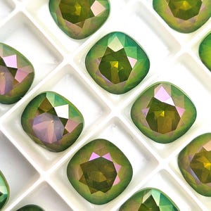 Peut inclure: Gros plan sur plusieurs pierres précieuses carrées vertes et violettes iridescentes. Les gemmes sont disposées dans une grille blanche, mettant en valeur leurs surfaces à facettes. Les gemmes ont une qualité réfléchissante, avec un mélange de teintes vertes, dorées et violettes.