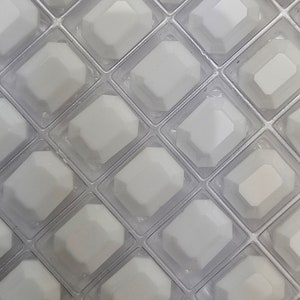 Op de afbeelding: Een close-up van een doorzichtige plastic mal met meerdere ruitvormige vakken. De mal is ontworpen om ijsblokjes of andere kleine bevroren lekkernijen te maken.