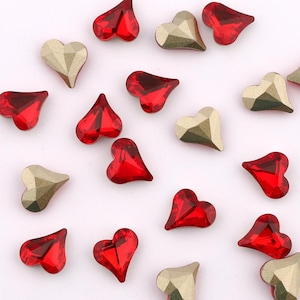 May include: Assortment of red and gold heart-shaped rhinestones. The rhinestones are scattered on a white background.