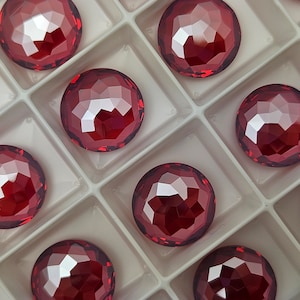 May include: A close-up of a tray of red, faceted, round gems. The gems are arranged in a grid pattern in a white tray.