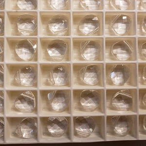 May include: A clear plastic tray filled with clear glass beads. The beads are arranged in a grid pattern and are all the same size and shape.