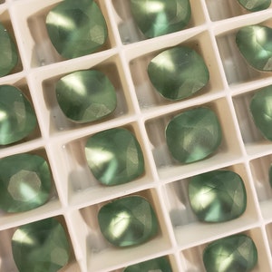 Può includere: Una vista ravvicinata di un vassoio di strass quadrati verdi. Gli strass sono disposti in un motivo a griglia e hanno una finitura lucida e iridescente.