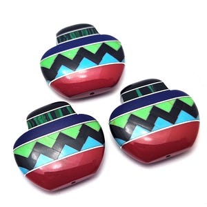 Puede incluir: Tres cuentas de cerámica de color rojo en forma de corazón con un patrón geométrico de negro, verde, azul y blanco. Las cuentas están hechas para parecer cerámica nativa americana.