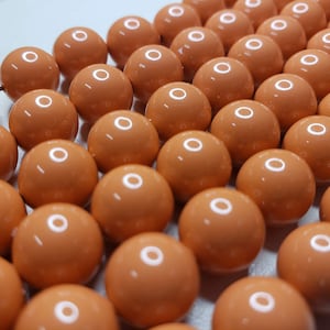 Puede incluir: Primer plano de una gran cantidad de cuentas redondas de color naranja. Las cuentas son lisas y brillantes.