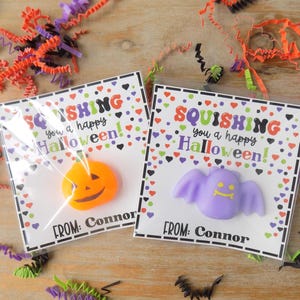 May include: Two clear plastic packages containing Halloween-themed squishy toys on white cards. One card features an orange pumpkin toy, the other a light purple bat toy. Both cards display the text SQUISHING you a happy Halloween! FROM: Connor.