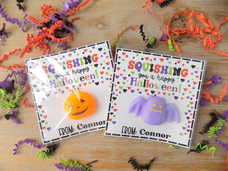 May include: Two clear plastic packages containing Halloween-themed squishy toys on white cards. One card features an orange pumpkin toy, the other a light purple bat toy. Both cards display the text SQUISHING you a happy Halloween! FROM: Connor.