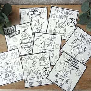 May include: A collection of black and white robot-themed birthday cards. Each card features a different robot design, along with the words "Happy Birthday" and "Robbie turns 8". The cards include balloons, wrenches, and birthday cakes.