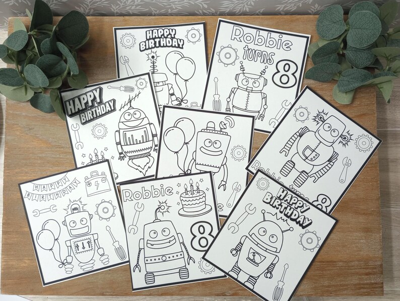 May include: A collection of black and white robot-themed birthday cards. Each card features a different robot design, along with the words "Happy Birthday" and "Robbie turns 8". The cards include balloons, wrenches, and birthday cakes.