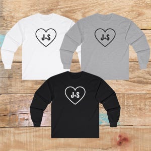 May include: Three long-sleeved shirts with a heart design and the text "J+S" in white. The shirts are white, grey, and black.