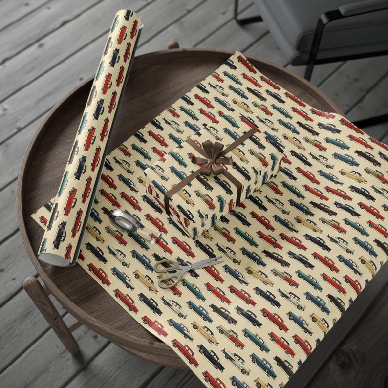May include: A vintage car wrapping paper design with a repeating pattern of colorful cars on a cream background. The paper is rolled up and a gift box is wrapped with the paper.