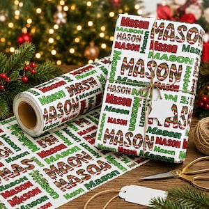 May include: A roll of white wrapping paper and a gift box wrapped in the same paper, both featuring the name Mason printed repeatedly in red, green, and a red-and-green striped pattern. The gift box is tied with twine and a star-shaped tag.
