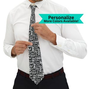 May include: A black and white tie with the word "Dad" repeated in a pattern. The tie is worn with a white dress shirt and black pants. The image includes the text "Personalize More Colors Available!"