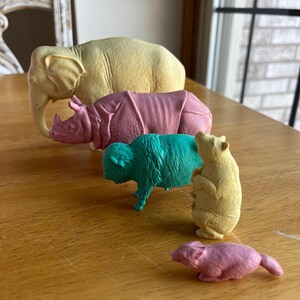 May include: A set of five colorful animal figurines, including an elephant, rhinoceros, bison, bear, and a smaller animal. The figurines are made of plastic and are arranged in order of size, with the largest figurine at the left and the smallest at the right.