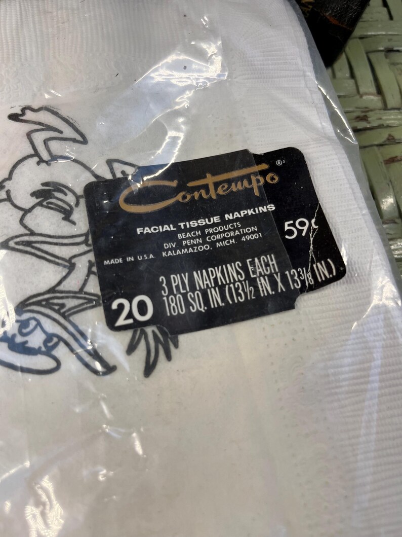 May include: A pack of 20 white facial tissue napkins featuring a cartoon character on the front. The pack is labelled "Contempo Facial Tissue Napkins" and "3 Ply Napkins Each 180 sq. in. (13 1/2 in. x 13 3/8 in.)".