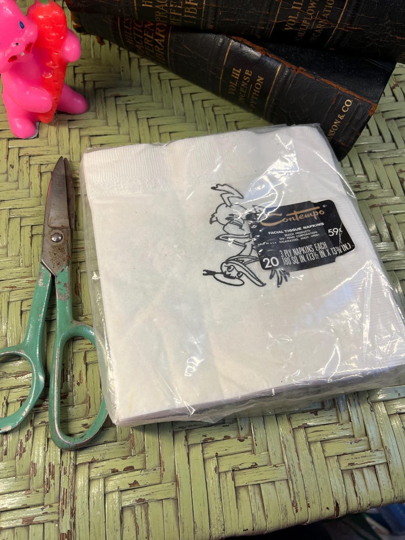 May include: A pack of 20 white Contempo facial tissue napkins. The pack is sealed in plastic and features a cartoon illustration of a bird wearing a hat. The text on the pack reads "Contempo Facial Tissue Napkins 59&cent; 3 Ply Napkins Each 180 sq in (13 1/8 in x 13 1/8 in)."