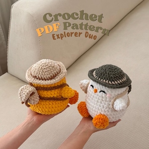 Può includere: Due animali di peluche all'uncinetto, uno giallo e marrone, l'altro bianco e grigio, ognuno con un cappello. Quello giallo ha le ali e il testo "Crochet PDF Pattern Explorer Duo" è sullo sfondo.
