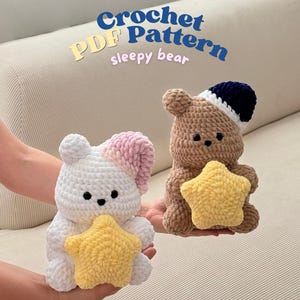 Può includere: Due orsetti di peluche all'uncinetto, uno bianco con una cuffia da notte rosa e uno marrone con una cuffia da notte blu scuro, che tengono ciascuno una stella gialla all'uncinetto. Il testo Crochet PDF Pattern sleepy bear è sopra i peluche.