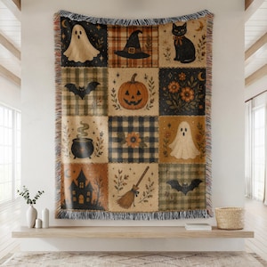 May include: A woven throw blanket featuring a grid of twelve square panels with Halloween imagery including ghosts, a black cat, a jack-o'-lantern, a witch hat, a broomstick, a haunted house, bats, and floral motifs in orange, black, and tan.