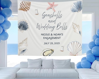 Puede incluir: Un telón de fondo de tela blanca con ilustraciones de acuarela de conchas marinas, una estrella de mar y campanas. El texto dice "Seashells and Wedding Bells" con los nombres "Nicole & Noah" y la fecha "July 29, 2025" para un anuncio de compromiso.