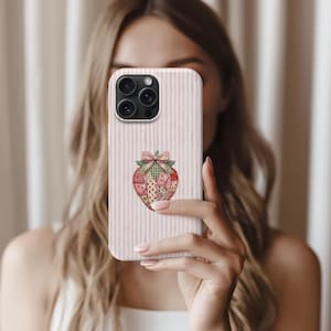 May include: A phone case with a pink and white striped pattern, showcasing a strawberry design. The strawberry is crafted from diverse patterned fabrics, such as red gingham, pink hearts, and green plaid, and is topped with a green bow. The case has a camera cutout.