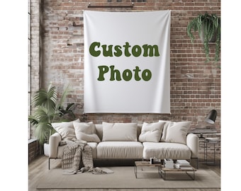 May include: A white wall hanging with the words "Custom Photo" in green script is displayed above a cream-colored sectional sofa. The room has a brick wall and is decorated with plants and a black lamp.