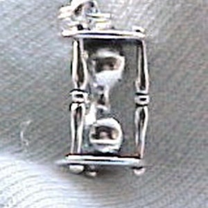 May include: Silver charm in the shape of an hourglass. The hourglass is made of metal and has a clear glass center. The charm is a great addition to any jewelry collection.