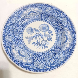 May include: A white ceramic plate with a blue and white floral pattern. The plate has a scalloped edge and a raised rim.